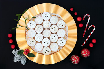Festive home made Christmas mince pies on a plate with holly, snow covered fir, mistletoe, cedar cypress, bow & loose berries on grey grunge background. Xmas food composition. Flat lay, top view.