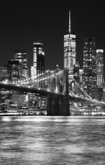 Black and white night view of Brooklyn Bridge and Manhattan waterfront, New York City, USA.