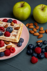 Belgian waffles on a pink plate with berries, almonds and apples.