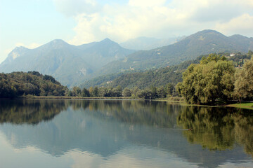 Fototapeta premium Beautiful panoramic view over a small Italian lake with the Alps in the distance. Photo was taken on a sunny day in summer.