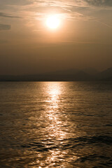 Naklejka premium Sunset at Garda lake, Italy. Sun behind clouds with reflections. 