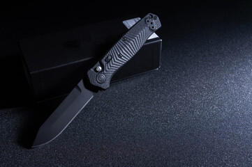 Lay the pocket knife at an angle on the box. Black knife at an angle.