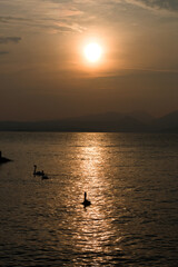 Sunset at Garda lake, Italy. Sun behind clouds with reflections. 