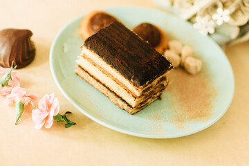 A piece of tiramisu tart in a green plate. Zephyr with chocolate and small pink carnations