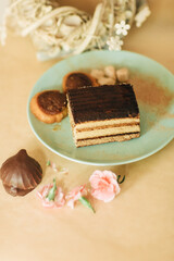A piece of tiramisu tart in a green plate. Zephyr with chocolate and small pink carnations