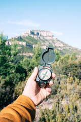 Close-up vertical shot from a hand holding a compass that points north with an unfocused mountain...