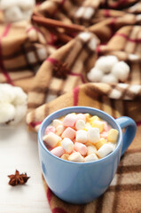 Cup of hot chocolate and marshmallows with plaid on grey wooden background.