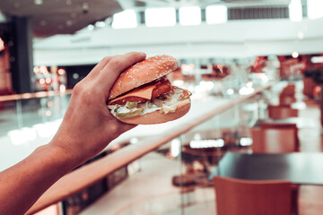 hamburger in the girl's hand on the background of the shopping center