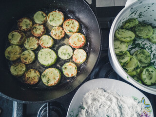 Sliced courgette zucchini cooking in a griddle frying pan on a hob stove