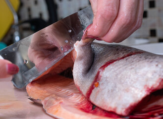woman in the kitchen peels fresh trout. fish cooking concept.