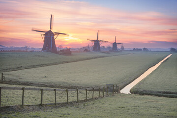 Three windmills and a fence at a winter sunrise