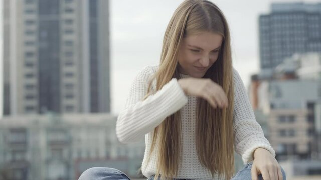 Portrait of ill young woman sneezing and rubbing nose. Beautiful careless Caucasian lady sitting on city square having symptoms of respiratory viral infection. Health care concept.