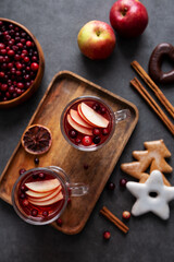 Top view hon cranberries juice with apple and spices, decorated with gingerbread, cinnamon and berries at dark background