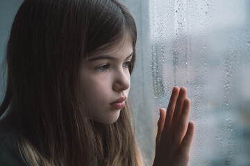 little, young sad girl at the window. Keeps his hand on the glass, lonely child depressed