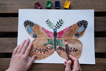 the child draws an unusual beautiful butterfly with watercolors and pencils
