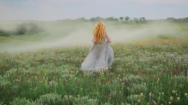young happy fantasy blonde woman queen runs, walks in green nature, whirls, dances fluttering skirt, gray dress waving in motion. Vintage summer clothes. Candid girl princess bride. Back rear view