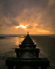 Offshore pipeline on the beach at sunset with sunshine breaking through the clouds