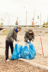 Two volunteers, young couple, tying up garbage bags after cleaning sea coast with trash pickers