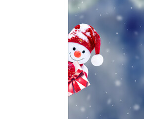Little snowman in cap with gift on snow in the winter. Background with a funny snowman. Christmas card.