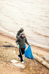 Two environmental volunteers, man and woman, with grabbers and garbage bags cleaning polluted sea coast