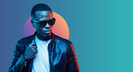 Banner of stylish black young man wearing leather jacket and sunglasses, isolated on blue gradient background - Powered by Adobe