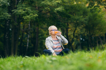 Beautiful senior woman on a walk in the park, performs exercises sitting on the grass, morning in...