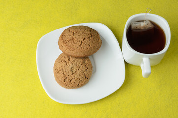Oatmeal cookies in a white plate with a mug of tea on a blurry yellow background.