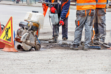 Fototapeta premium Three road service people with manual road tools are repairing a section of the road.