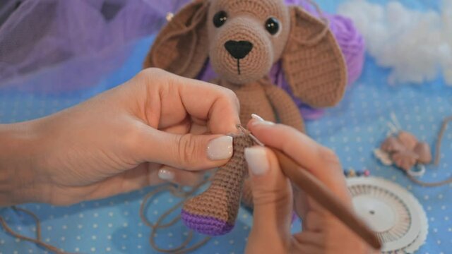 Handicraft master. crochet a paw for a plush puppy. The toy is waiting for its paw in the background. Crochet toys master class. workplace of needlewoman. hobby, handicraft, handiwork