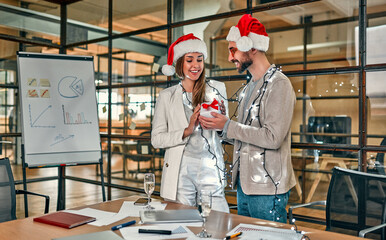 Happy New Year and Merry Christmas! Two young creative people wearing Santa hats exchange gifts on the last working day.