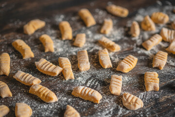 Hand made raw gnocchi di patata,traditional Italian potato noodles ready for cooking on wooden table. Selective focus, close up view, copy space. Vegan food. Process of cooking.