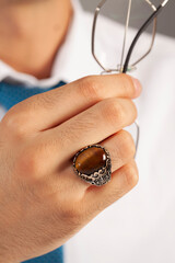 Brown silver ring and accessories on male finger in white shirt and blue tie.