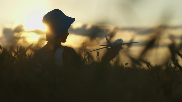 funny boy playing with airplane in the golden wheat field at sunset, boy dreams of being a pilot