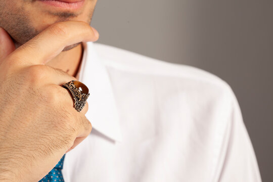 Brown silver ring and accessories on male finger in white shirt and blue tie.