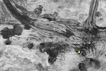Heavy machines, including isolated yellow trucks, in the working environment in a mine, seen in an aerial, black and white photo taken from a drone. Working quarry environment