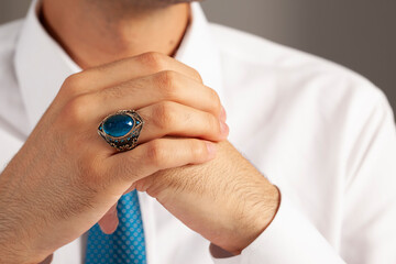 Blue silver ring and accessories on male finger in white shirt with blue tie.