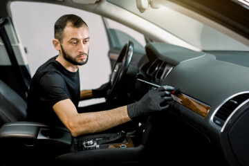 Close up of the process of removing dust with a brush during car interior cleaning. Young Caucasian man, car detailing service worker, cleaning car dashboard. Focus on hands with brush