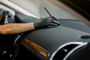 Car detailing and car wash concept. Cropped horizontal image of hand of car wash worker, cleaning gaps in the interior of the modern vehicle control panel, using the brush