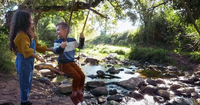 Small girl pushing boy on tree swing in the woods
