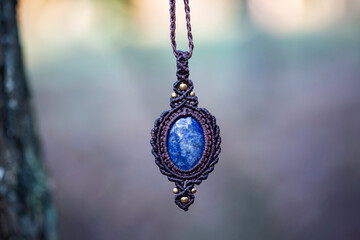 Mineral lapis lazuli gemstone ornamental pendant on blury forest background