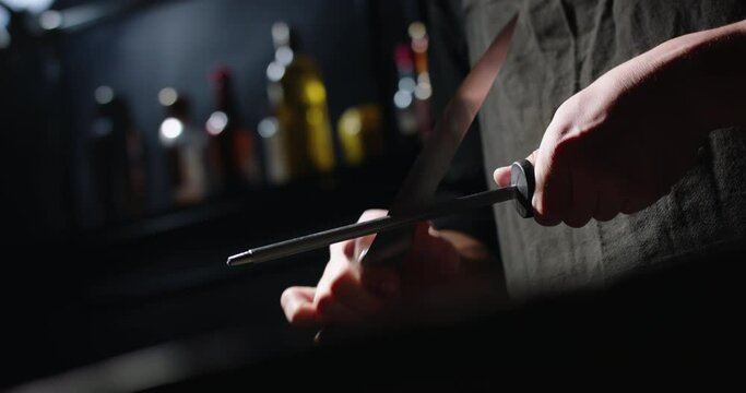 Professional chef is sharpening his knife before cooking a meal. Cool cooker is preparing his tools - food cooking concept close up 4k footage