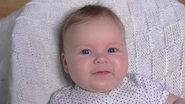 Little cute blue-eyed baby on a white blanket is laughing happily at the camera