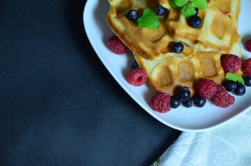 Homemade Belgium Waffles with fresh blueberries for breakfast. White plate, Viennese waffles with raspberries and mint. quick delicious breakfast on black background. top view copy space