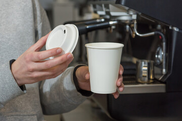 Paper cup with a lid in the hands of the barista