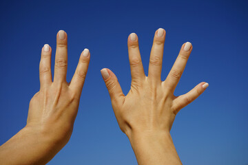 women's hands show the number eight against a cloudless blue sky