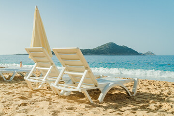 Empty Beach chairs and a yellow sun umbrella await tourists against the backdrop of the blue sea. Beautiful seashore beach resort.