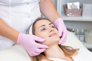 Fototapeta na wymiar Cosmetological facial massage. beautician doing facial massage to a satisfied beautiful young woman