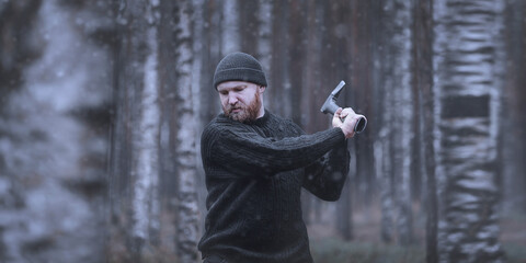 A brutal bearded man (woodman, forester, villager) cuts down a tree with an axe. Late autumn or...