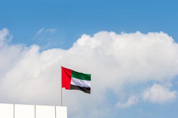 Flag waving at the top of the modern building, national symbol of United Arab Emirates. National Day and UAE flag day concept.