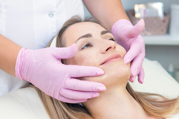 Obraz na płótnie Canvas Cosmetological facial massage. beautician doing facial massage to a satisfied beautiful young woman